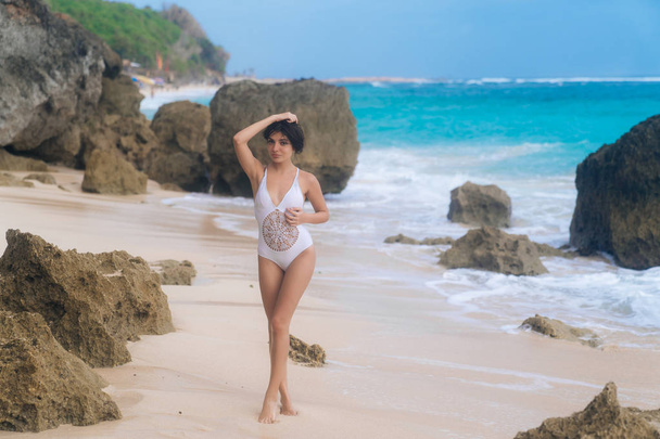 Beautiful sexy woman in white swimwear posing and tanned on summer vacation at rocky beach - Valokuva, kuva