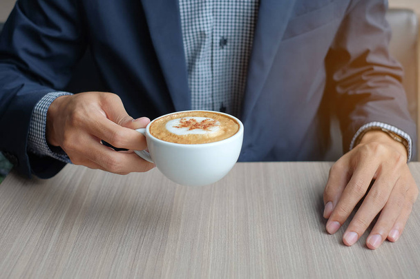 Zakenman holding en warme koffie drinken in office - Foto, afbeelding