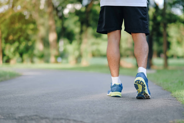 young fitness man legs running in the park outdoor, male runner walking on the road outside, asian athlete jogging and exercise on footpath in sunlight morning. Sport, healthy and wellness concepts - Photo, Image
