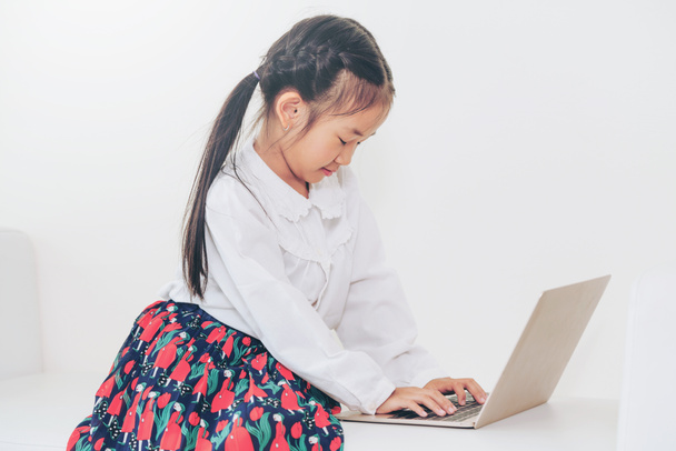 Маленька щаслива дитина, використовуючи ноутбук, сидить на білому дивані. Дитячий спосіб життя
. - Фото, зображення