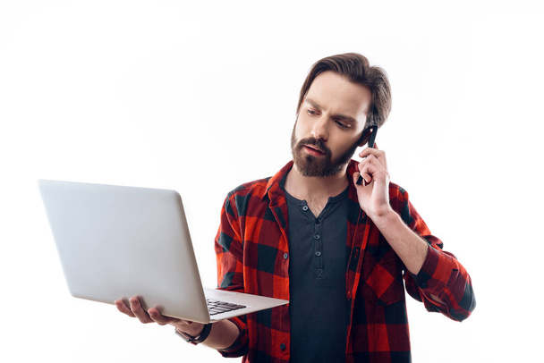 Bearded Man Working on Laptop and Talking on Phone - Foto, imagen