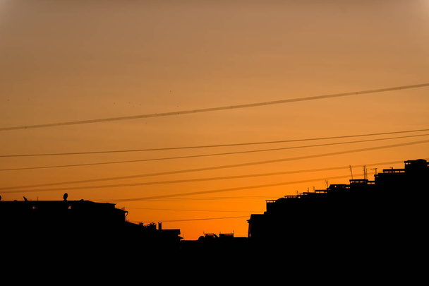Orangefarbener Sonnenuntergang in der Stadt. die Dächer von Hochhäusern. elektrische Kabel und Drähte. Abendblick auf die Stadt. Sonnenuntergang. - Foto, Bild