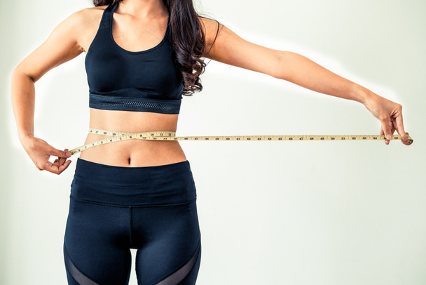 Primer plano de mujer con cuerpo delgado midiendo su cintura y torso. Nutrición saludable y pérdida de peso concepto. - Foto, imagen