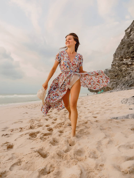 Gelukkige vrouw in zomerjurk op strand bij zonsondergang of zonsopgang. Vrouwelijke stijl. - Foto, afbeelding
