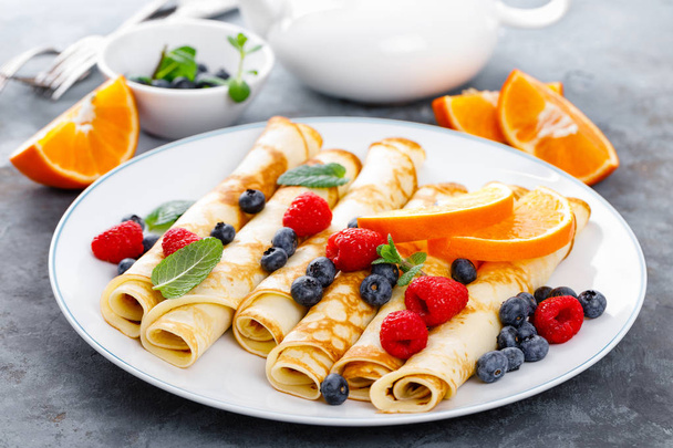 Panqueques dulces envueltos con bayas frescas, crepes con arándanos y frambuesas para el desayuno
 - Foto, Imagen