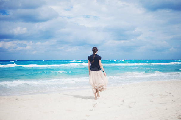 Back view of young woman in a long skirt walking on the ocean.  - Fotoğraf, Görsel