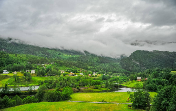 Beautiful Norway nature landscape with small house and village in the middle of valley surrounded by green hills and mountain - Foto, afbeelding
