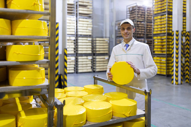 un hombre con una bata blanca con una cabeza de queso en sus manos está en un almacén de queso
 - Foto, imagen