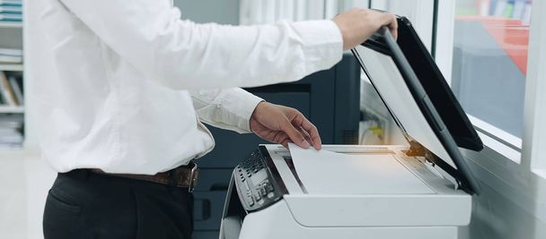 Bussiness άνθρωπος χέρι βάζοντας ένα χαρτί έγγραφο σε εκτυπωτή σαρωτή ή λέιζερ μηχανή αντίγραφο στο γραφείο - Φωτογραφία, εικόνα