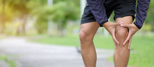 若いフィットネス抱きかかえたスポーツ足の怪我、筋肉トレーニング中に痛みを伴う。アジアのランナーがランニングと運動後の膝の痛みや問題を持つ夏の外 - 写真・画像