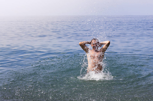 Mann jubelt und spritzt in den Sommerferien Wasser ins Meer - Foto, Bild
