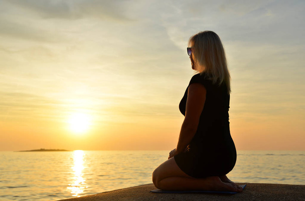Frau sitzt in Yoga-Pose am Meer bei Sonnenuntergang. - Foto, Bild