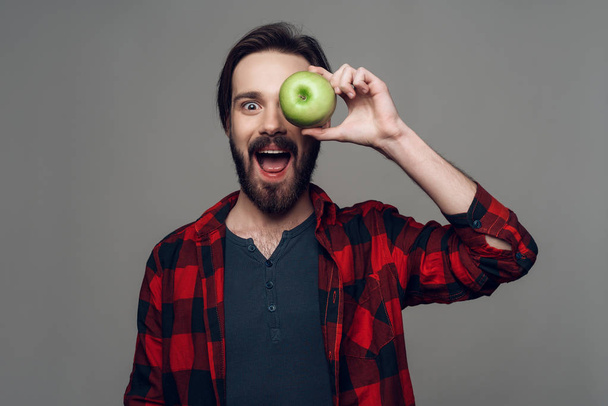 Happy bearded man hold Apple and looking at Camera. Man in Checkered Shirt Looking at Camera with Amazed Expression. Isolated on Gray Background. Concept of People Emotions - Foto, immagini
