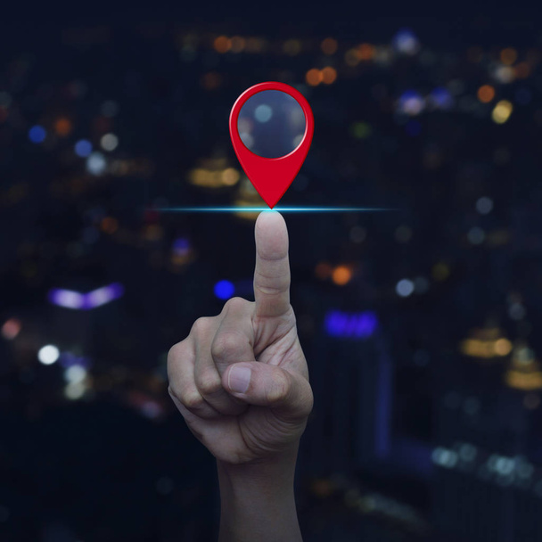 Hand pressing map pin point location button over blur colourful night light city tower, Map pointer navigation concept - 写真・画像