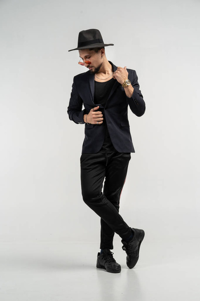 Fashion portrait of handsome elegant man in black suit and hat posing in studio - Foto, Bild