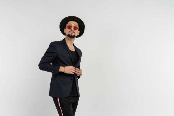 Half length portrait of young handsome serious modern male wearing black suit and hat in round sunglasses - Photo, Image
