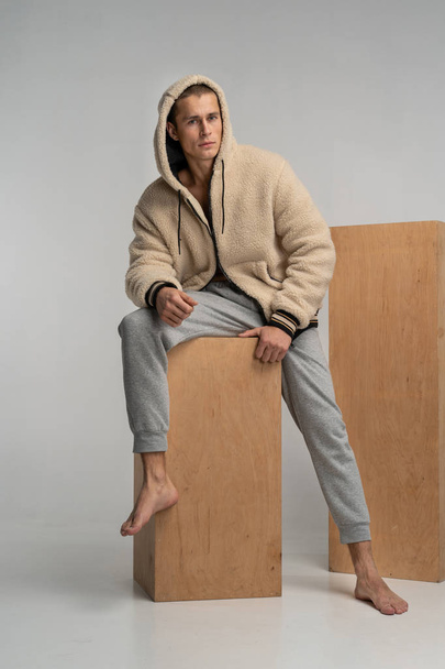 Мужская модель в спортивной форме, сидящая на деревянном кубе, смотрит в сторону
 - Фото, изображение