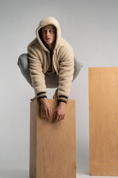 Slimme ernstige jonge man in sportwear crouched houten kubus en poseren - Foto, afbeelding