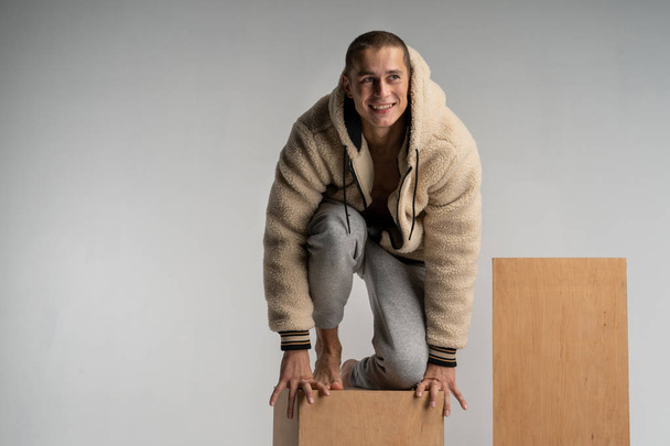 Se krčil na dřevo kostka a představují inteligentní usměvavý mladý muž v sportwear - Fotografie, Obrázek
