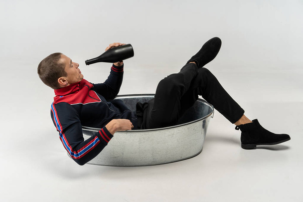 Handsome model male with short haircut in casual wear sitting in the metal bath - Zdjęcie, obraz