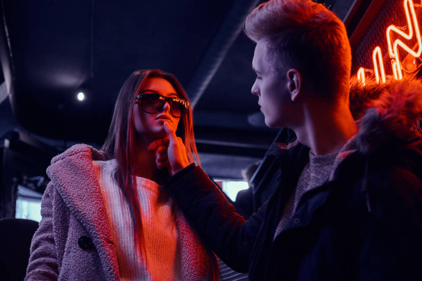 Portrait of a passionate young couple looking at each other in the underground nightclub with the industrial interior, he gently touches her chin - Фото, изображение