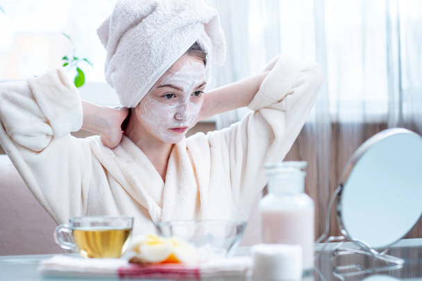 Beautiful happy young woman with cosmetic natural mask on her face looking at her skin. Concept skin care and Spa treatments at home - Foto, Imagen