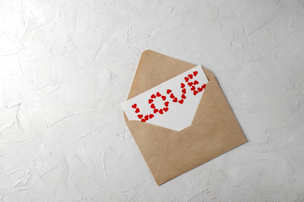 Valentines day minimal concept, hanmade gift - craft envelope, love note, word love made of small red paper hearts on gray background - 写真・画像