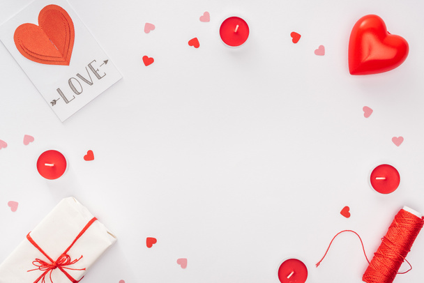 top view of gift box, paper hearts and greeting card with 'love' lettering isolated on white with copy space, st valentines day concept - Fotoğraf, Görsel