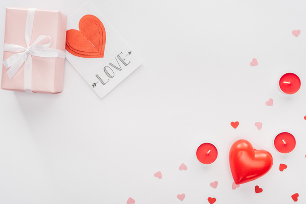 top view of gift box, paper hearts and greeting card with 'love' lettering isolated on white, st valentines day concept - 写真・画像