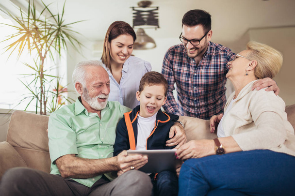 Portret van een drie-generatie familie tijd samen doorbrengen thuis met behulp van digitale tablet. - Foto, afbeelding