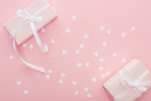 top view of gift boxes with ribbons and paper hearts isolated on pink - 写真・画像
