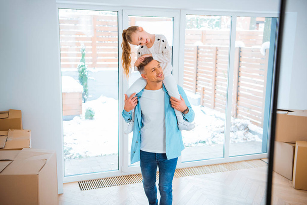 schöner Vater trägt am Hals lächelnde Tochter beim Spazierengehen im neuen Zuhause - Foto, Bild