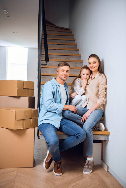 happy family smiling while sitting on stairs in new home - Photo, Image