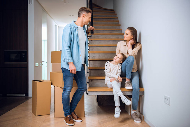 hombre guapo mirando a la hija y la esposa sentado en las escaleras en el nuevo hogar
  - Foto, imagen