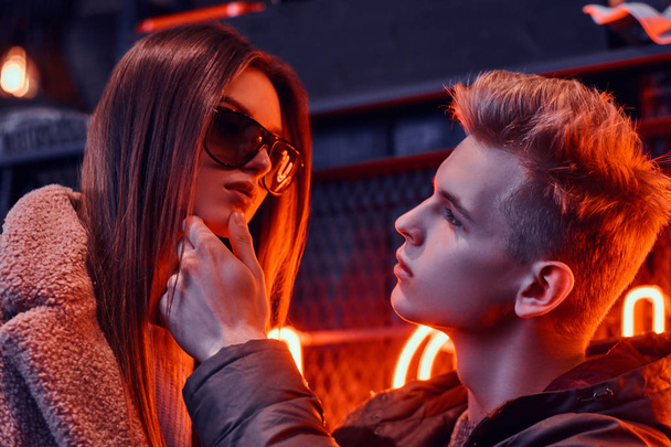 Close-up portrait of a passionate young couple looking at each other in the underground nightclub with industrial interior, he gently touches her chin - Photo, image