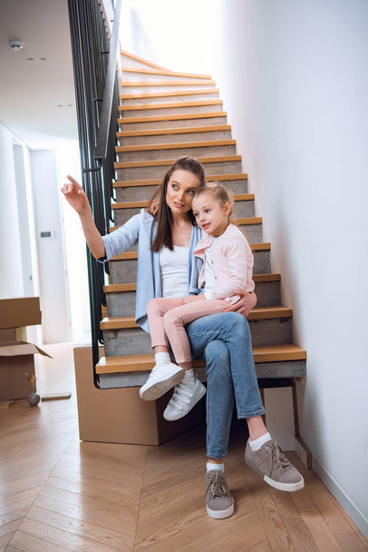 kızıyla merdivenlerde oturan ve yeni ev parmak işaret çekici kadın  - Fotoğraf, Görsel