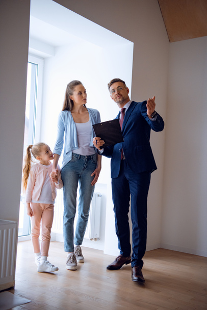 handsome broker showing room while standing near attractive woman and kid - Photo, Image