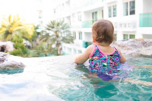 bambino guarda in lontananza nella piscina all'aperto sullo sfondo di alberi di cocco e il paesaggio, piscina a sfioro
, - Foto, immagini