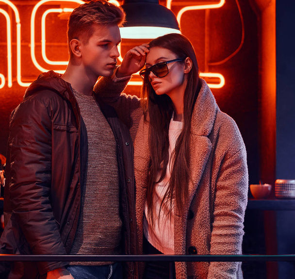 Attractive young couple wearing in stylish clothes standing together in a cafe with industrial interior - Фото, изображение