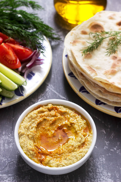 Vegan food, homemade hummus with flatbread, vegetables and olive oil on a concrete background. Selective focus. - Foto, afbeelding