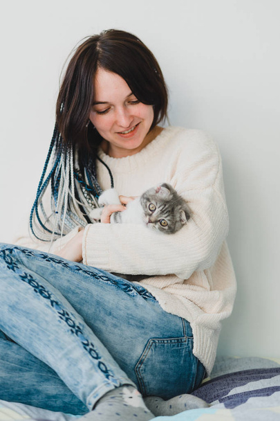 Jolie jeune fille dreadlock souriante avec un petit chaton dans ses mains dans la chambre confortable
   - Photo, image