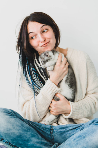 Kaunis hymyilevä nuori rastatyttö pieni kissanpentu käsissään viihtyisässä makuuhuoneessa
   - Valokuva, kuva
