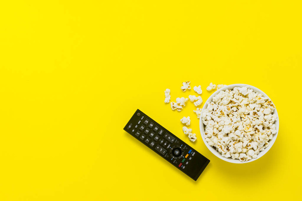 A bowl of popcorn and TV remote on a yellow background. The concept of watching TV, film, TV series, sports, shows. Flat lay, top view - Photo, Image