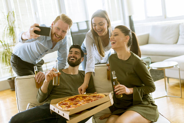 Grupo de jóvenes tomando selfie con teléfono móvil en la fiesta de pizza en la habitación
 - Foto, imagen