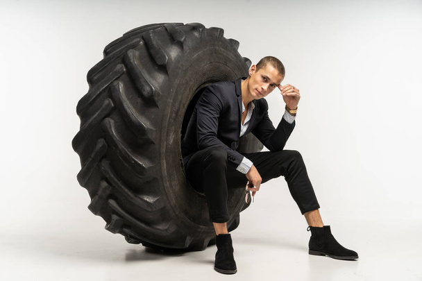 Stylish handsome man in black suit sitting in tire - Foto, afbeelding