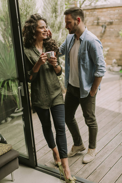 Happy young cute couple in love embracing each other and drinking coffee at home by the window - Foto, afbeelding