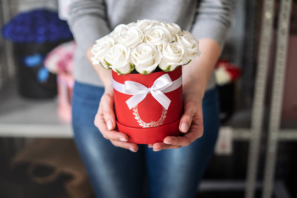 A bouquet of white rose buds in a round red box with a white ribbon in the careful hands of a girl. - Foto, Imagem