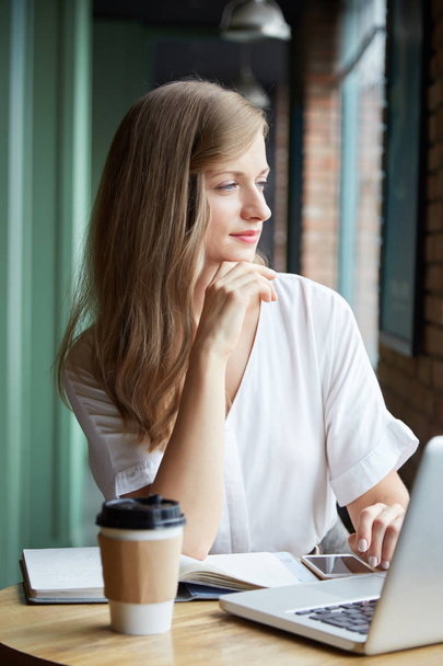 mujer mirando hacia otro lado y sentada en la mesa con portátil y café
  - Foto, imagen