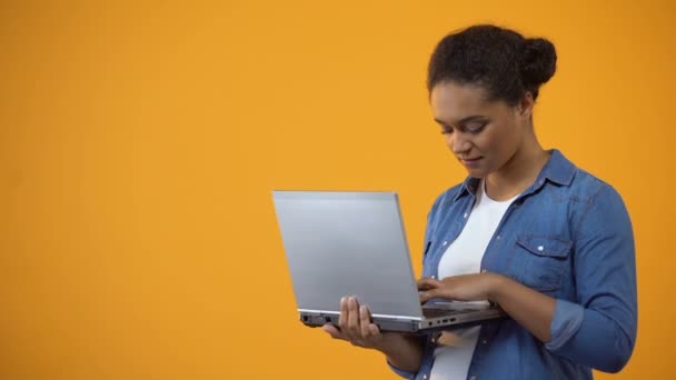 Pretty african american woman typing on laptop, isolated yellow background - Footage, Video