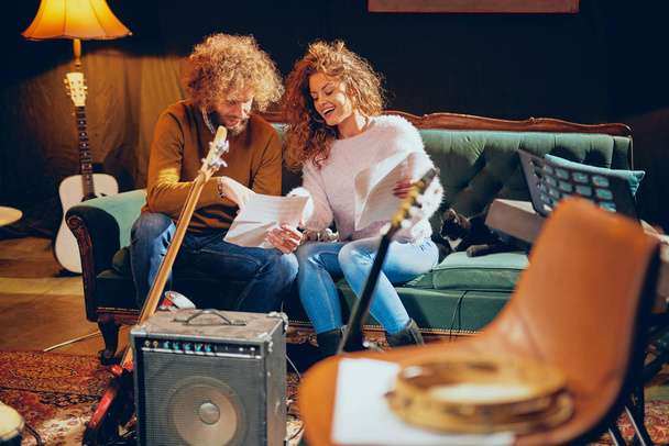 Woman and man with curly hair looking at notes and preparing for the gig. Home studio interior. - Foto, immagini
